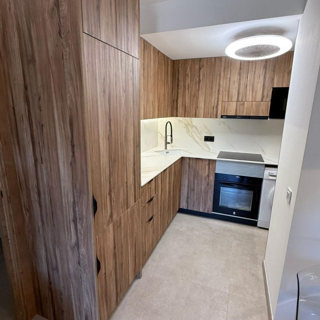 Modern kitchen with tall wood cabinets, marble countertop, black pull-down faucet, and integrated oven and induction hob.
