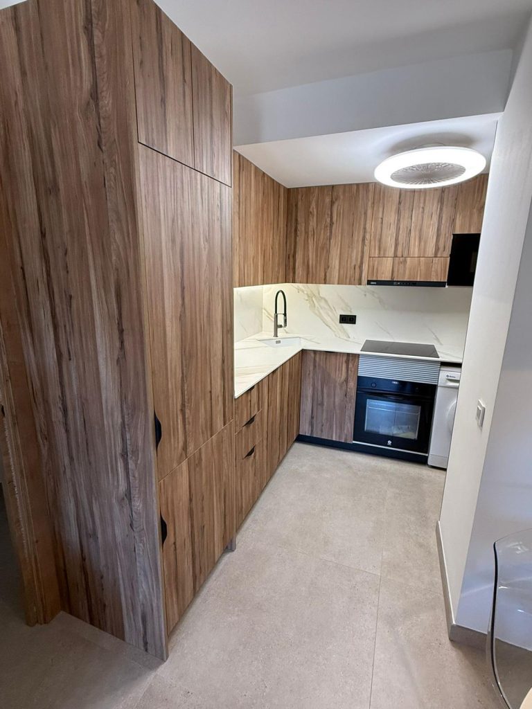 Modern kitchen with tall wood cabinets, marble countertop, black pull-down faucet, and integrated oven and induction hob.